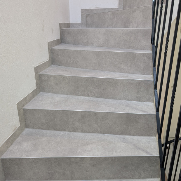 Eine geschwungene Treppe. Mit einem CV-Bodenbelag neu eingekleidet. Trennung der Setz- und Trittstufe durch ein Aluminiumprofil.